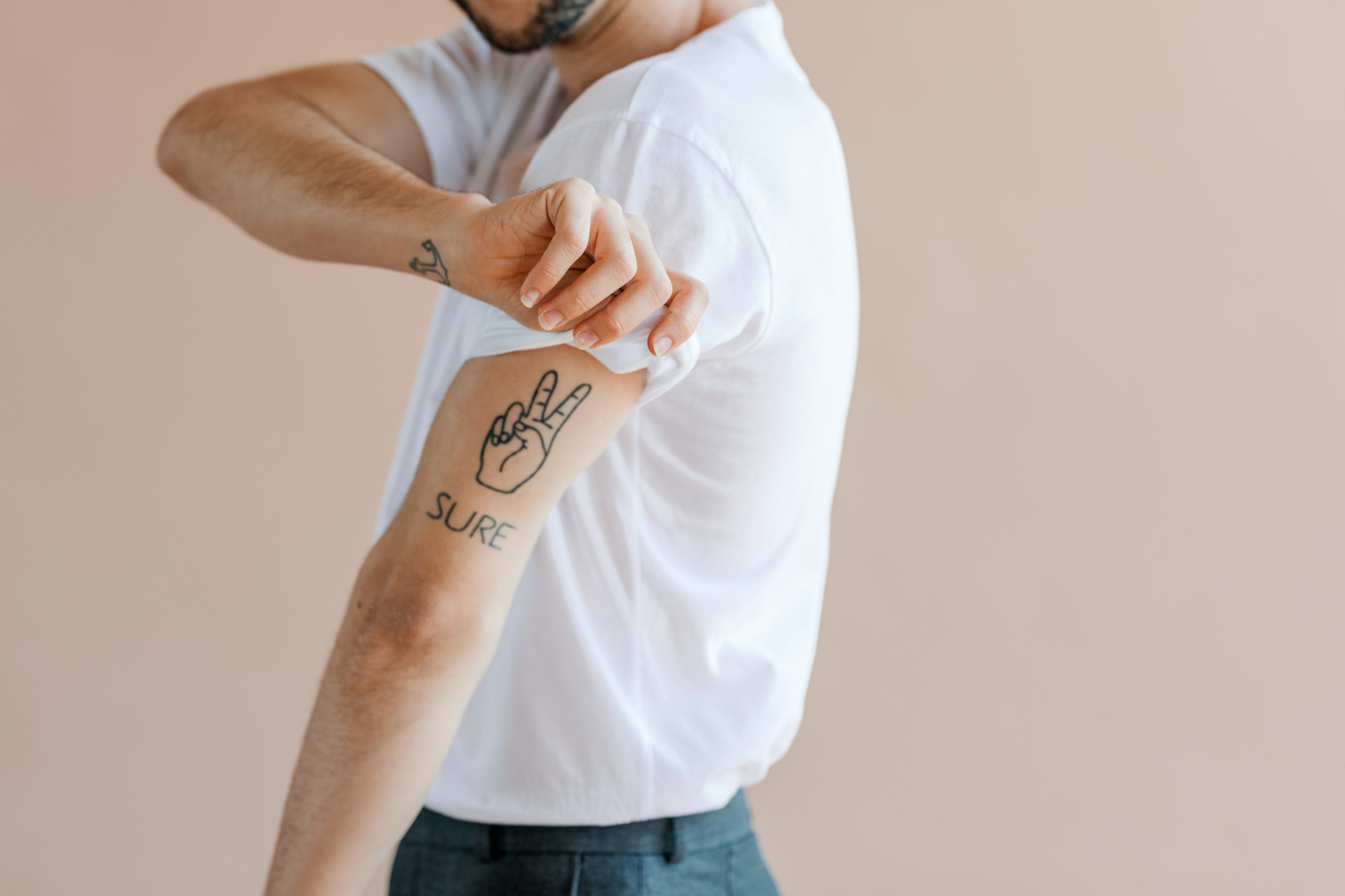 Person with arm tattoo of a hand making a peace sign and the word &quot;SURE,&quot; wearing a rolled-up sleeve shirt