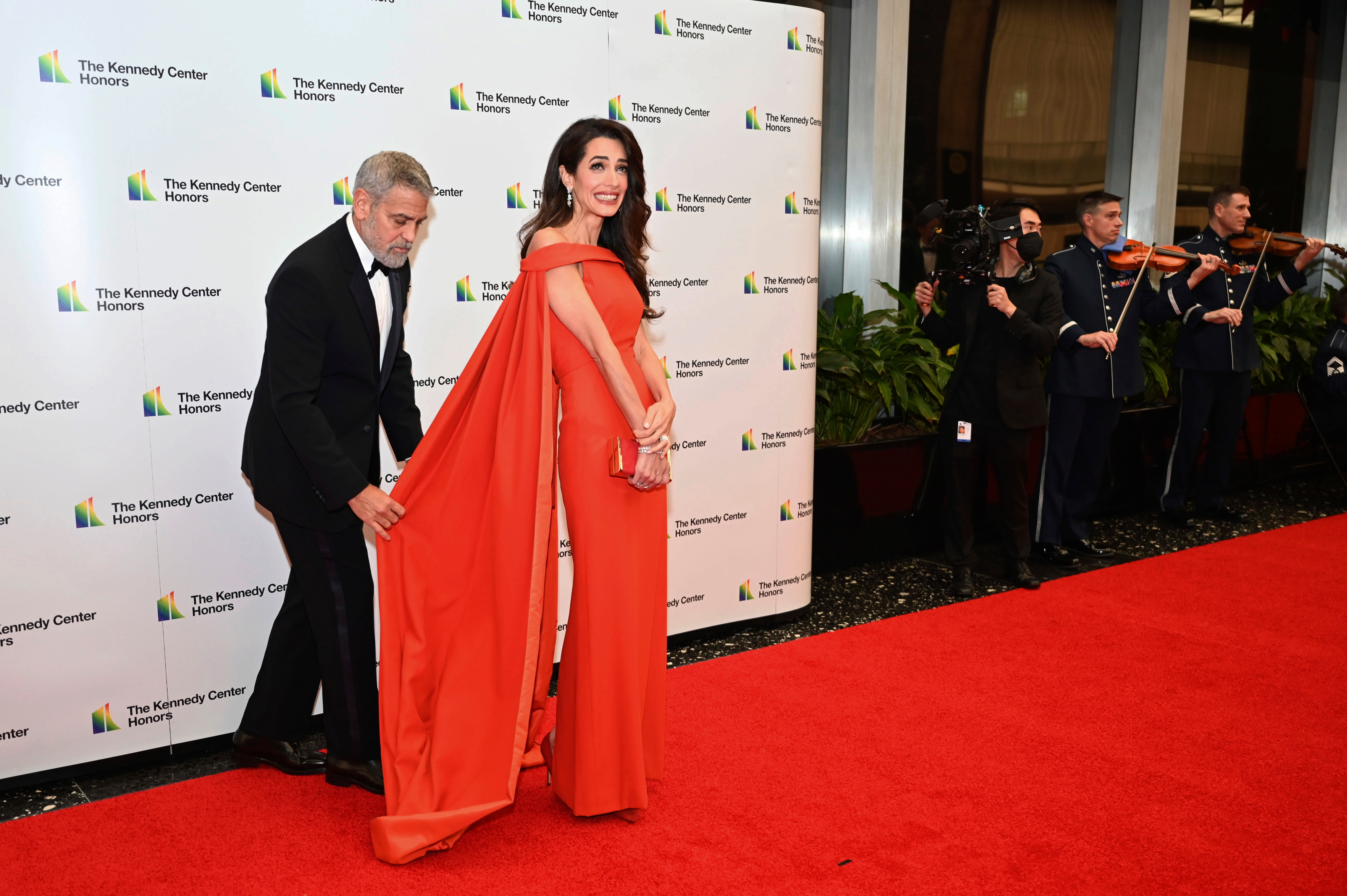 George, wearing a tux, adjusts the long train on the back of Amal's off-the-shoulder gown