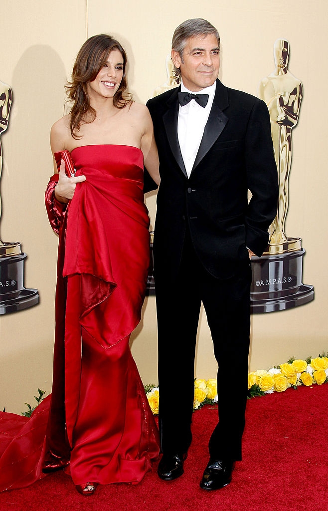 George in a classic tuxedo and Elisabetta in an elegant strapless gown pose together on a red carpet at an awards event