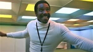 Person in a white turtleneck energetically extends arms in a bright, indoor setting