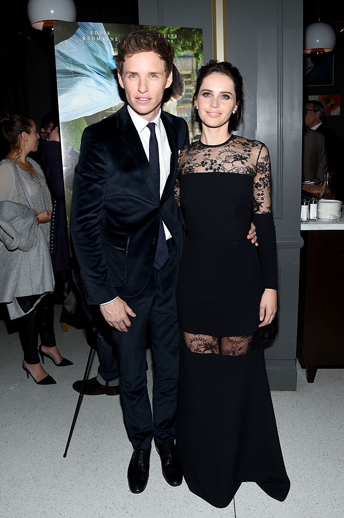 Eddie in a velvet tuxedo, and Felicity in a long dress with lace detailing, posing together near a movie poster