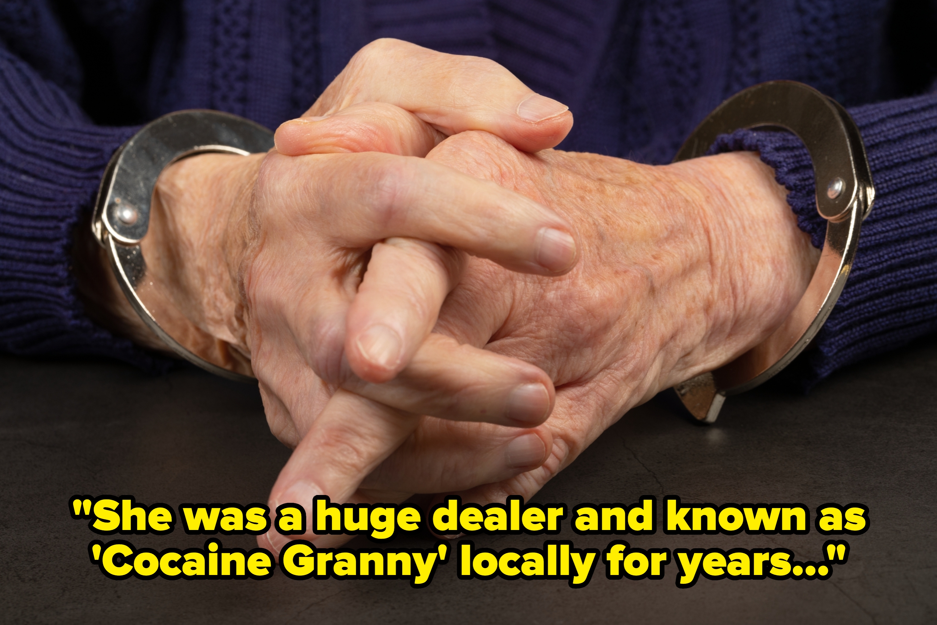 An elderly person's hands are clasped on a table, wearing handcuffs