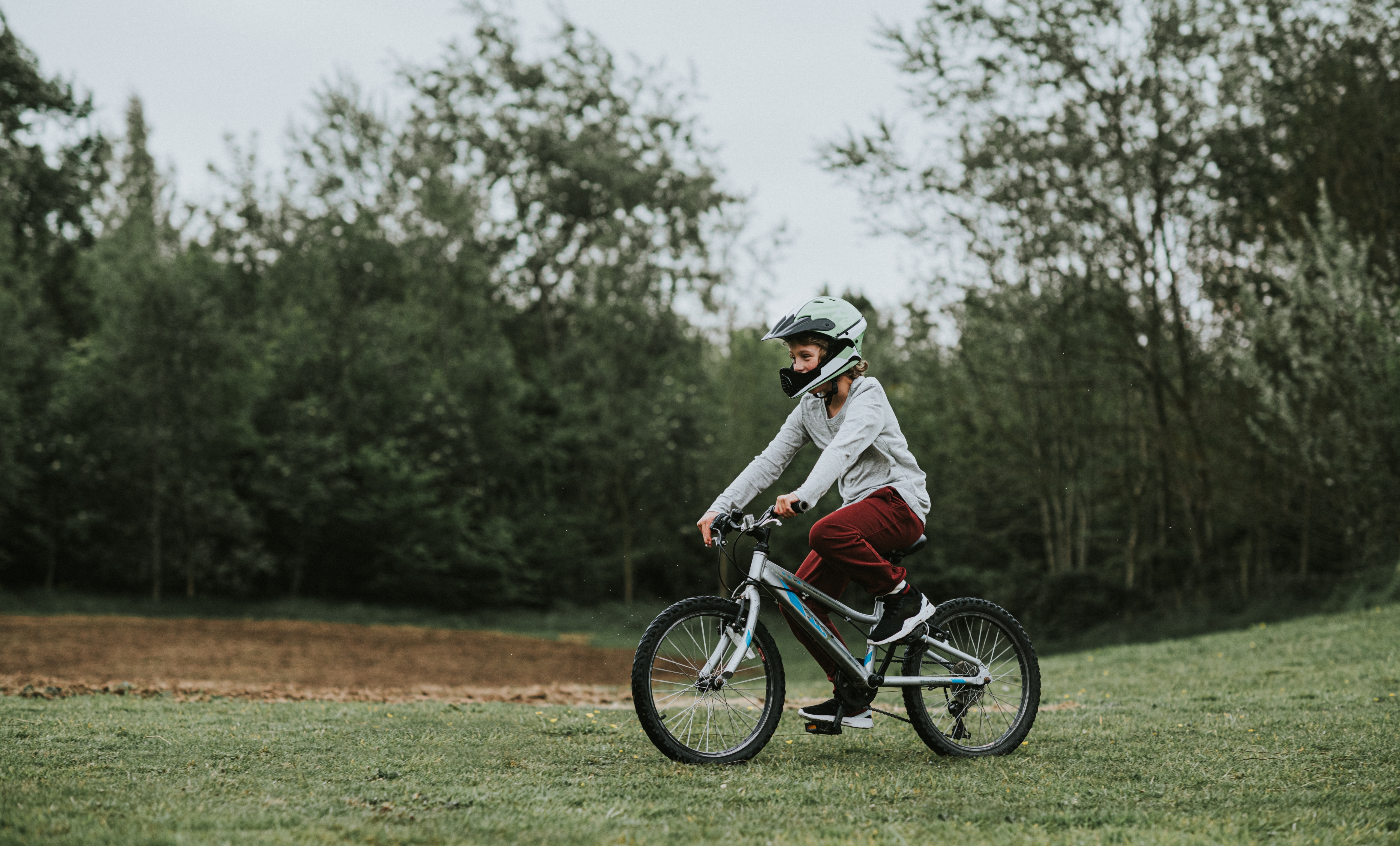Person cycling on grassy field with trees in background, wearing a helmet and casual clothing