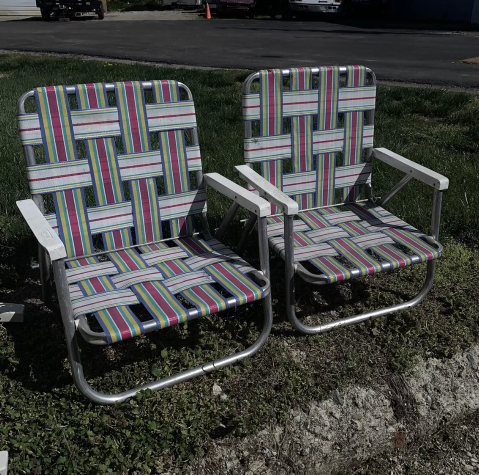 Two woven lawn chairs with a striped pattern sit on grass, facing forward. They're positioned next to each other in an outdoor setting