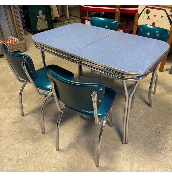 Retro dining set with a blue Formica table and four matching blue chairs, featuring chrome accents, in a vintage room setting