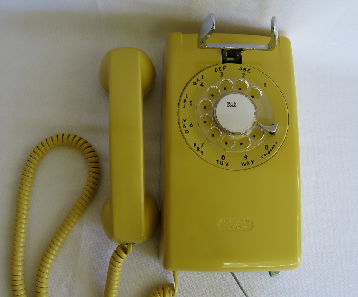 Yellow rotary dial telephone with handset and coiled cord placed on a flat surface