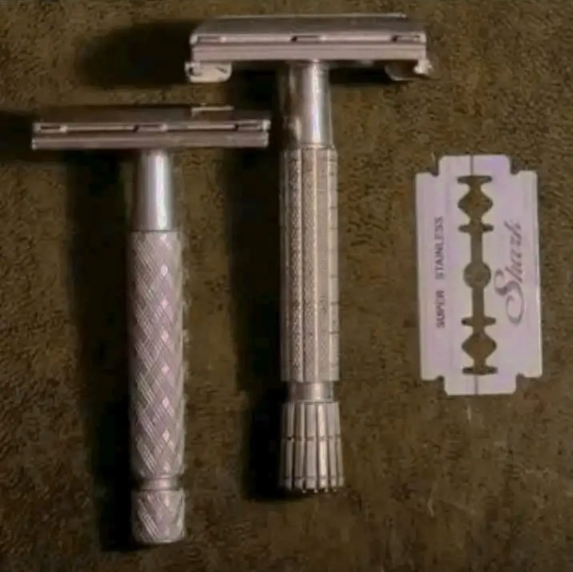 Two vintage safety razors with textured handles are displayed alongside a single razor blade on a surface