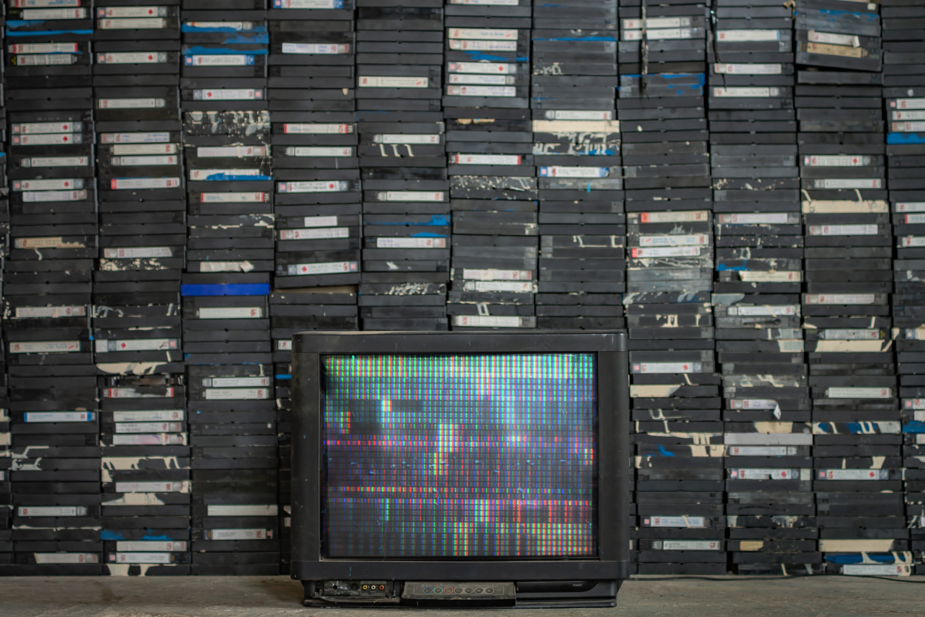 A vintage TV displaying static sits in front of a large, organized stack of VHS tapes, capturing a nostalgic media collection scene