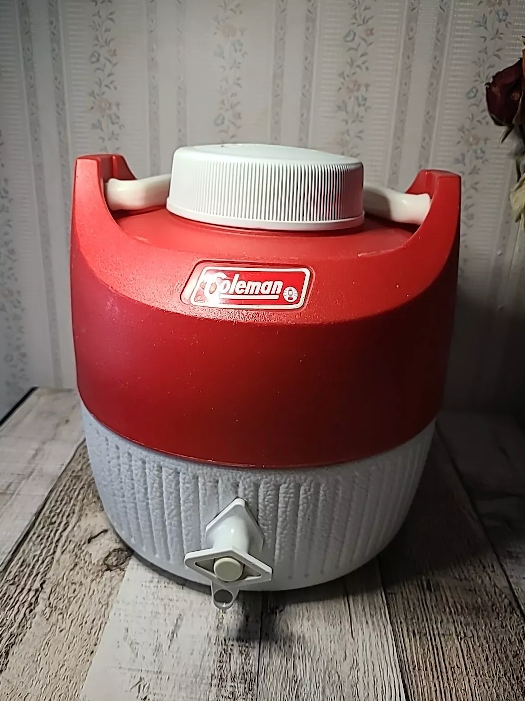 Vintage Coleman water cooler with spout, set on a rustic wooden surface