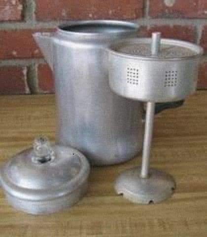 Metal stovetop coffee percolator with lid and basket components displayed on a wooden surface