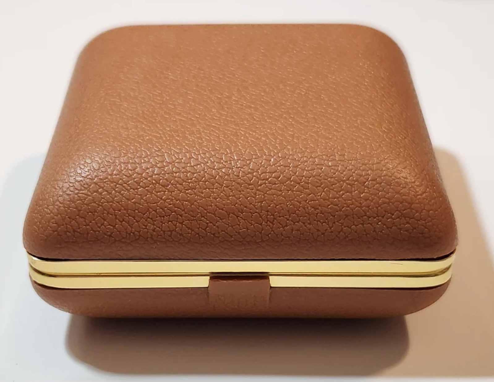 Closed brown leather jewelry box with gold trim, resting on a flat surface