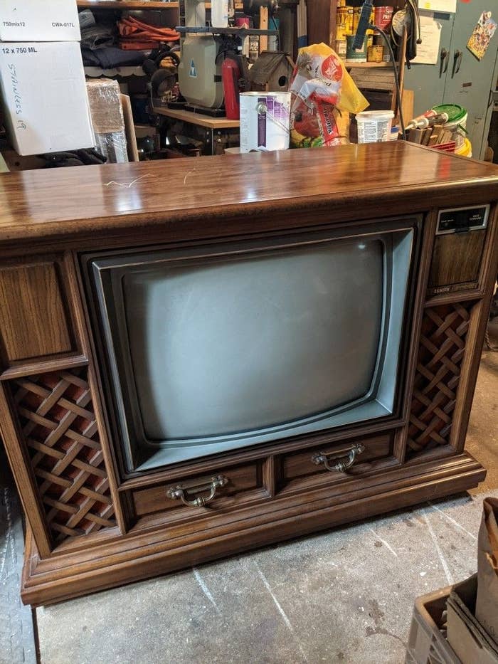 Vintage console TV with wood cabinet, lattice speaker covers, and control knobs, set in a cluttered garage
