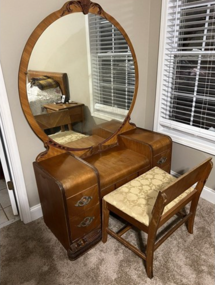 Vintage wooden vanity set with a circular mirror, ornate carvings, and a cushioned bench in a carpeted room