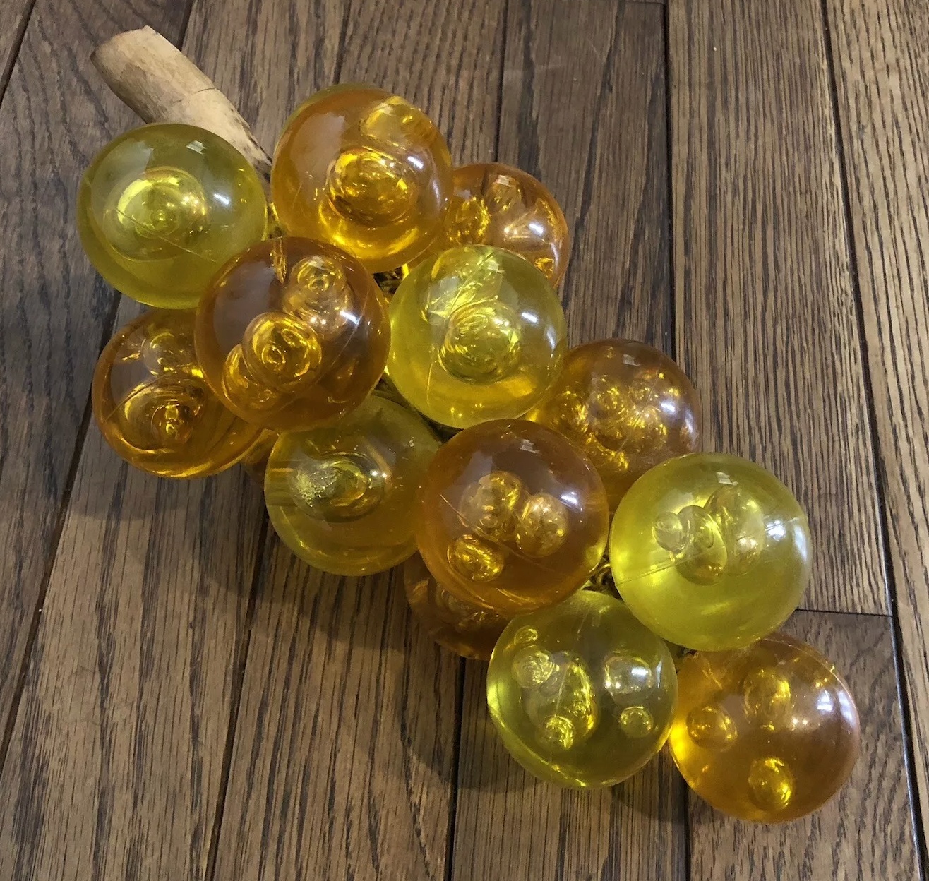 A cluster of transparent glass spheres resembles grapes on a stem, placed on wooden flooring
