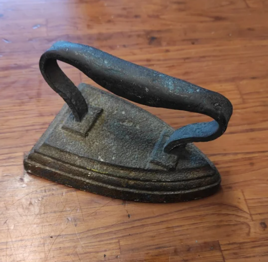 A vintage metal iron with a curved handle sits on a wooden surface