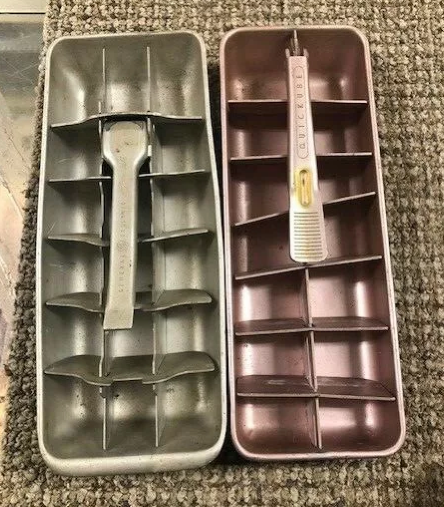 Two vintage metal ice cube trays with lever handles placed side by side on a textured surface