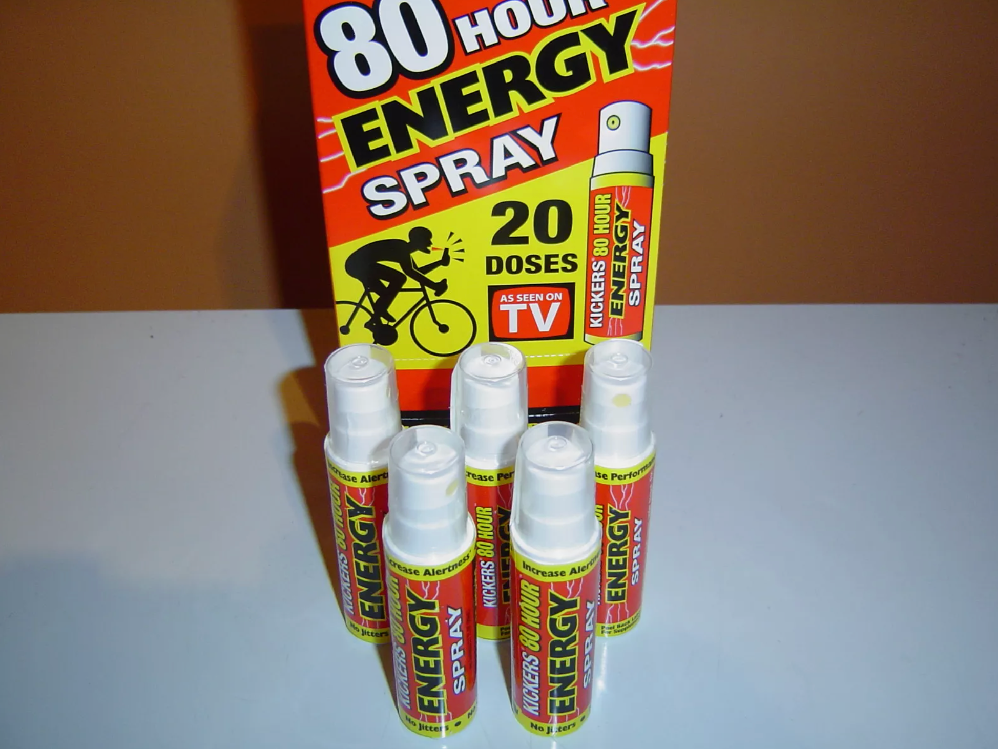 Five bottles of "80 Hour Energy Spray" are in front of a display box promising 20 doses per bottle and featuring a cyclist graphic