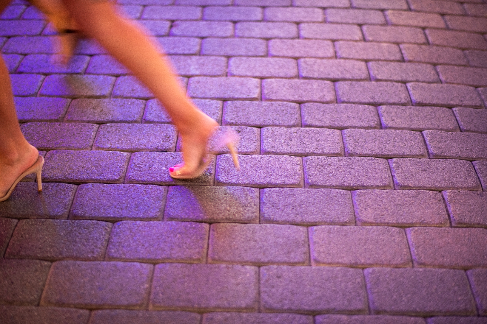 Person wearing high heels walking on a cobblestone path. Only legs and feet are visible
