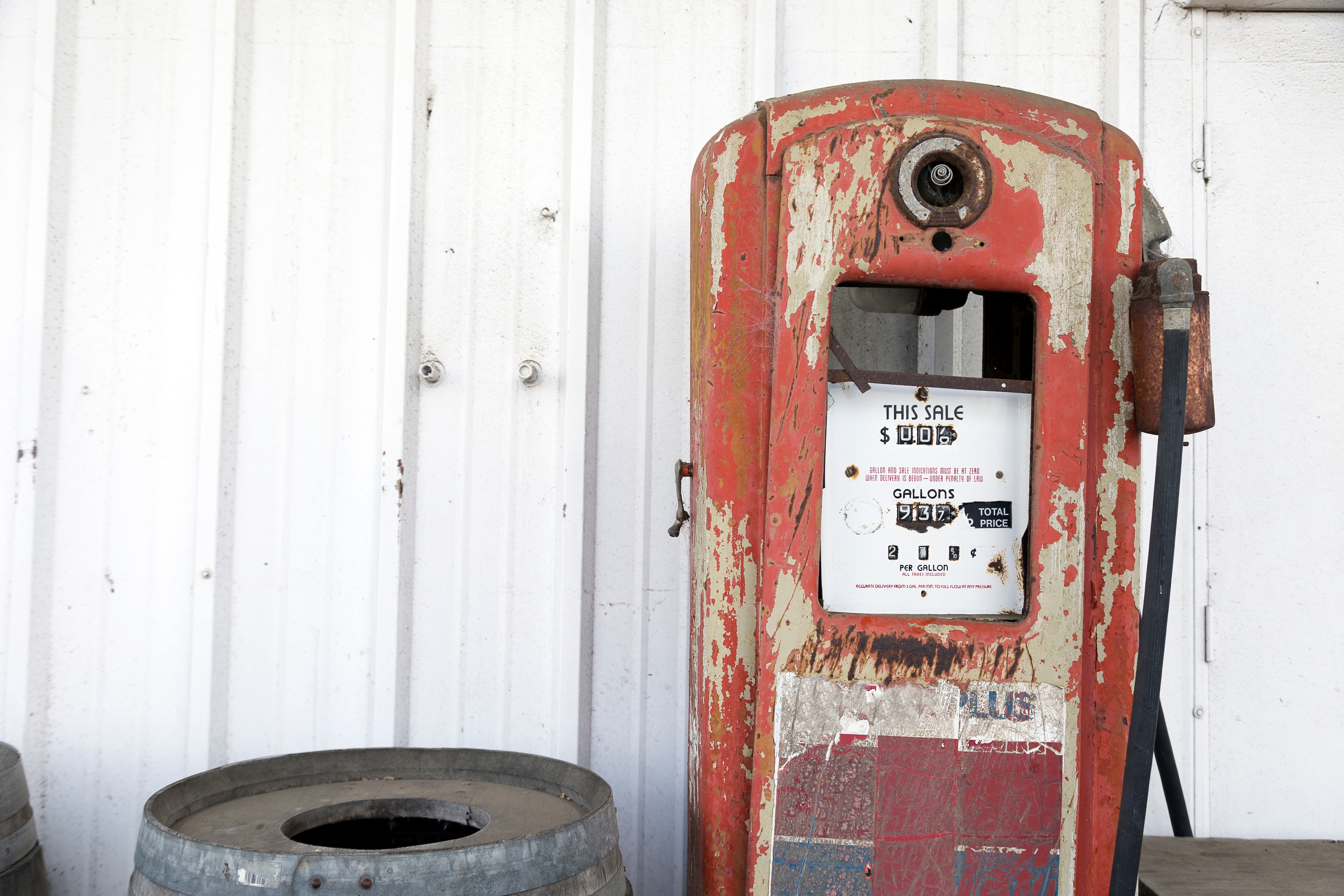 Weathered vintage gas pump next to a wooden barrel in front of a corrugated metal wall