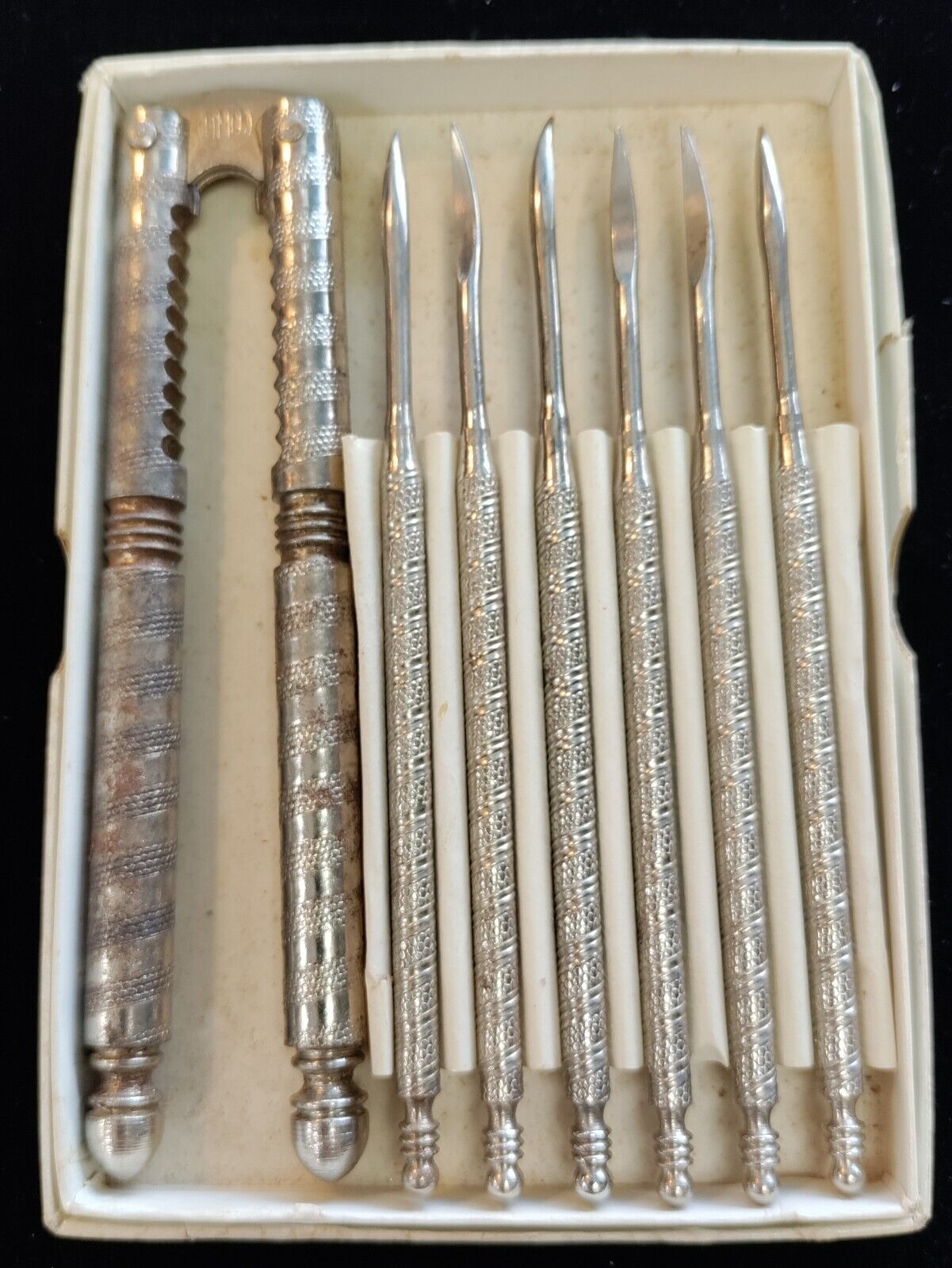 A vintage shaving kit with a single-edge razor and seven metal tools in a box, showcasing intricate handle designs