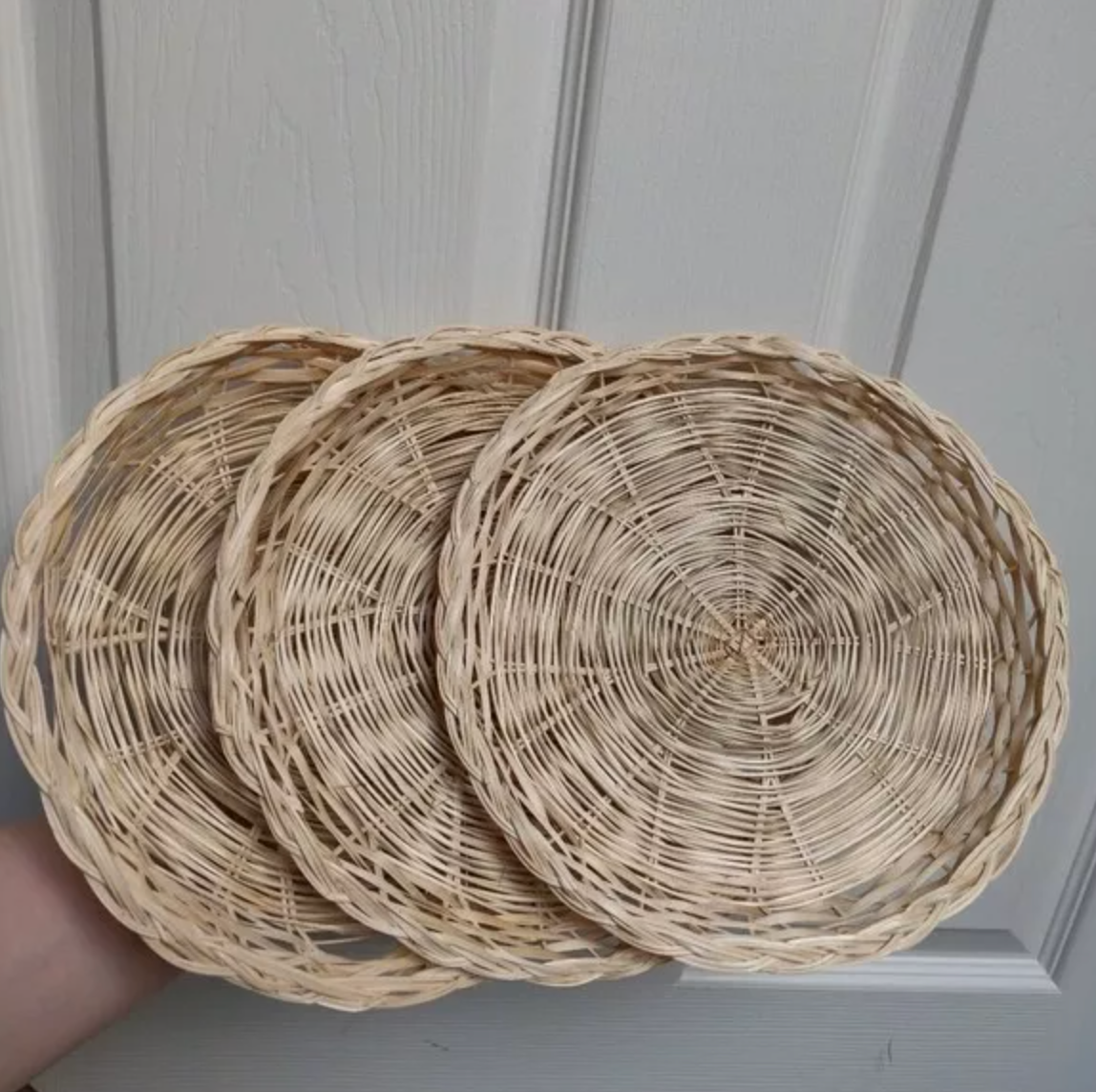 Three round, woven wicker baskets stacked and held in a hand against a door background