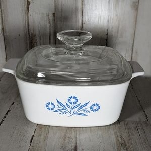 A vintage glass-lidded casserole dish with blue floral pattern, sitting on a rustic wooden surface