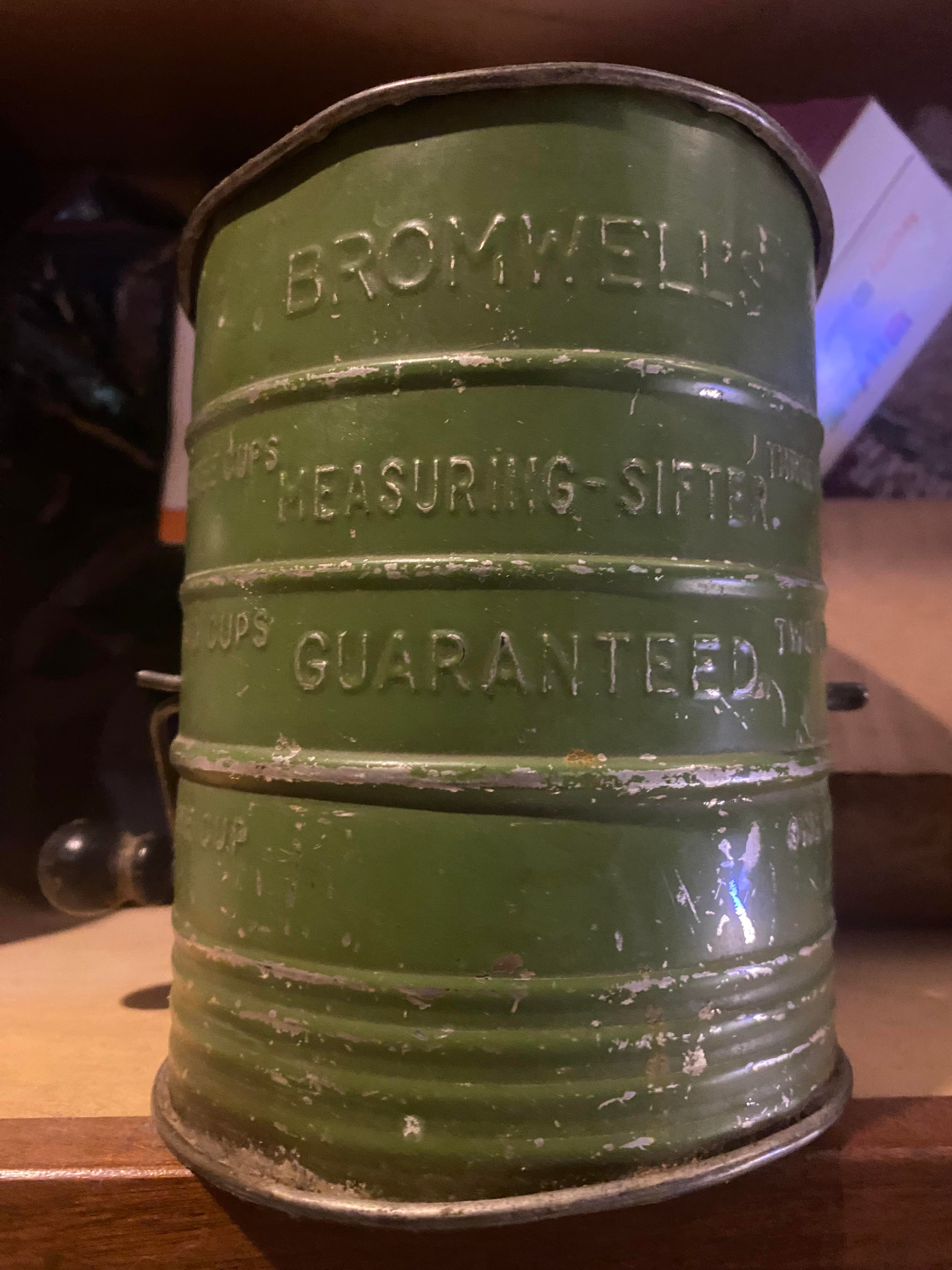 Green vintage Bromwell's flour sifter with embossed measurements displayed on a kitchen shelf