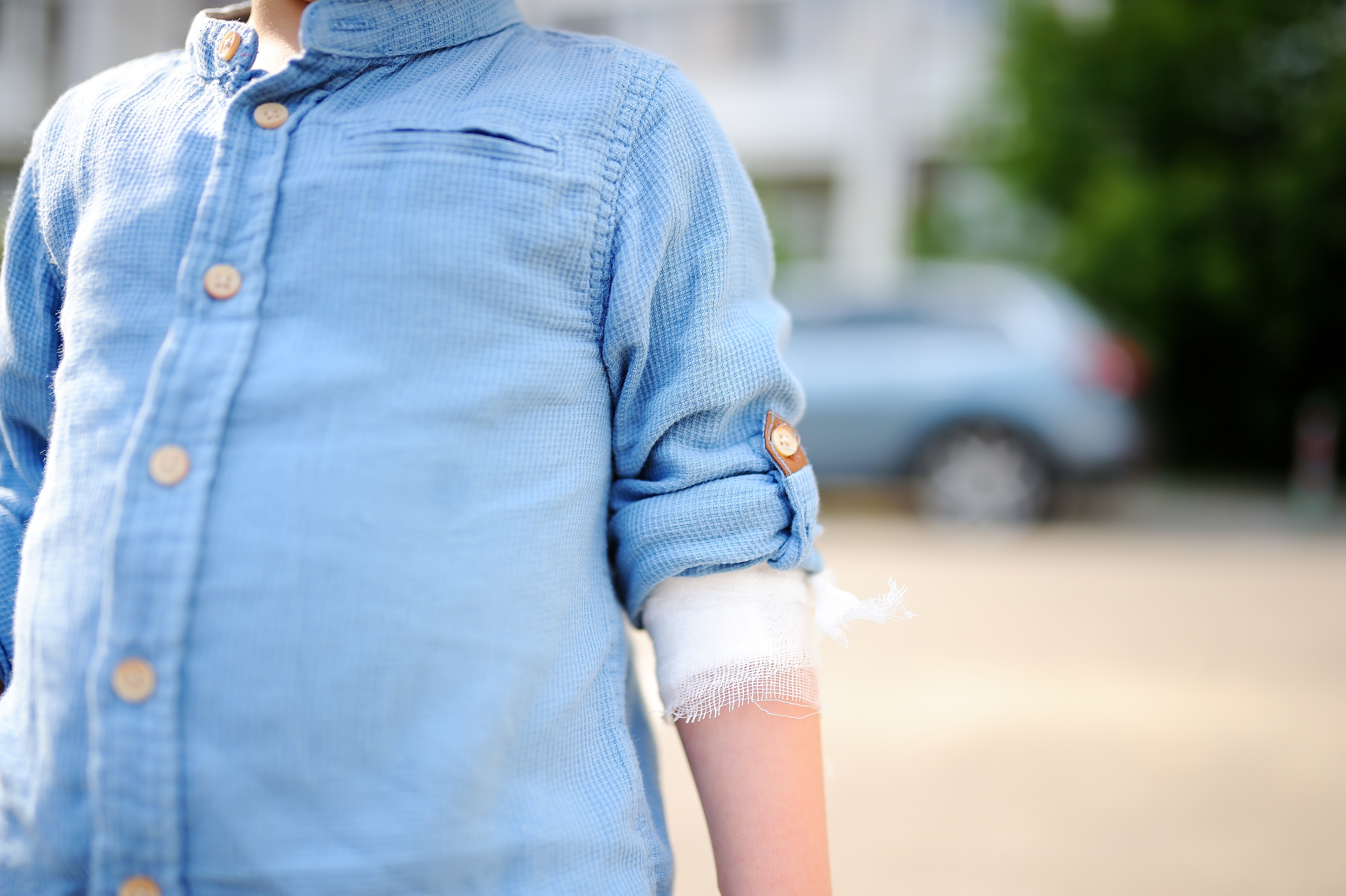 Child in rolled-up shirt with bandaged arm, standing outdoors