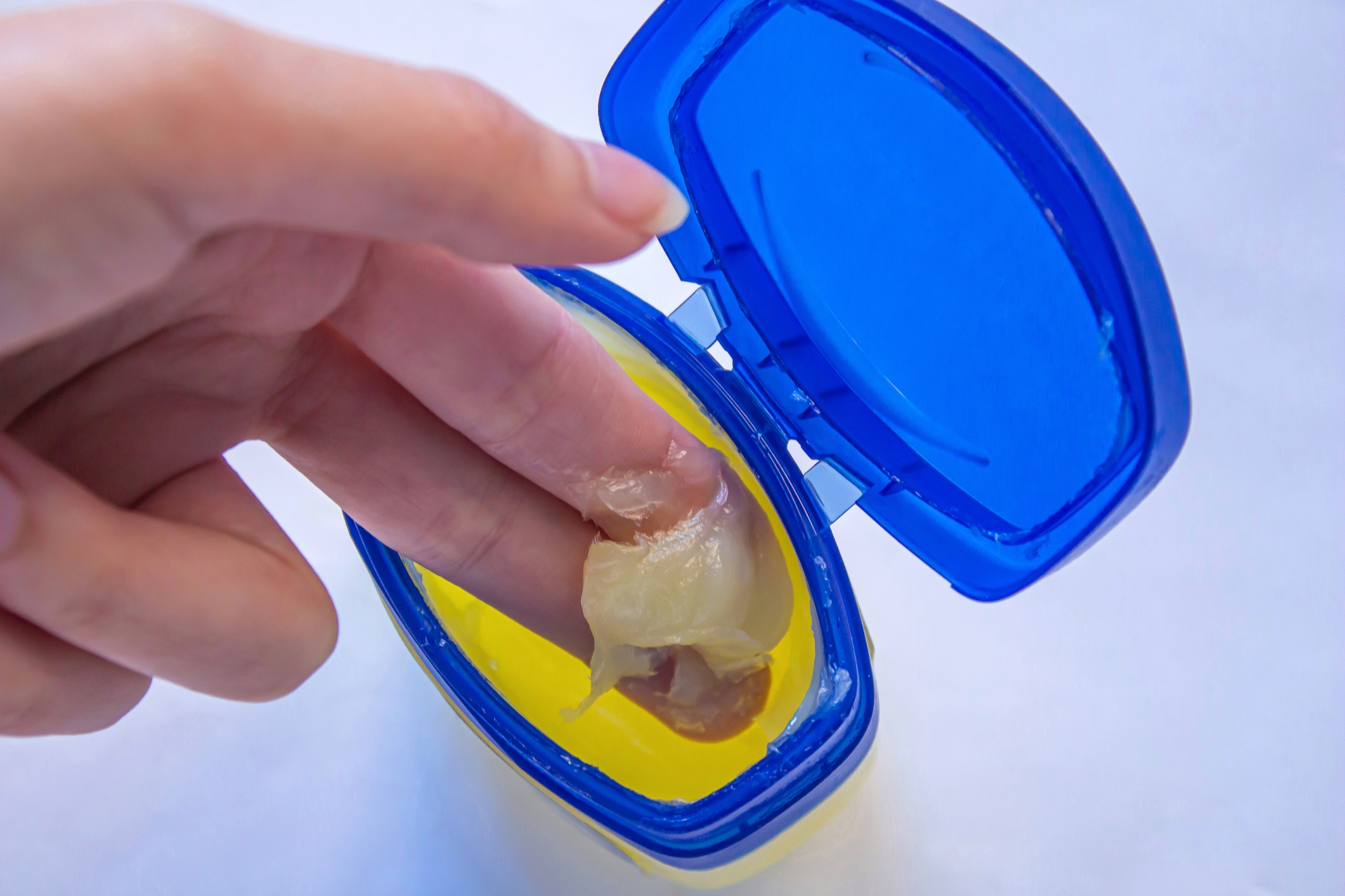 Open container of petroleum jelly with a person’s fingers scooping some out