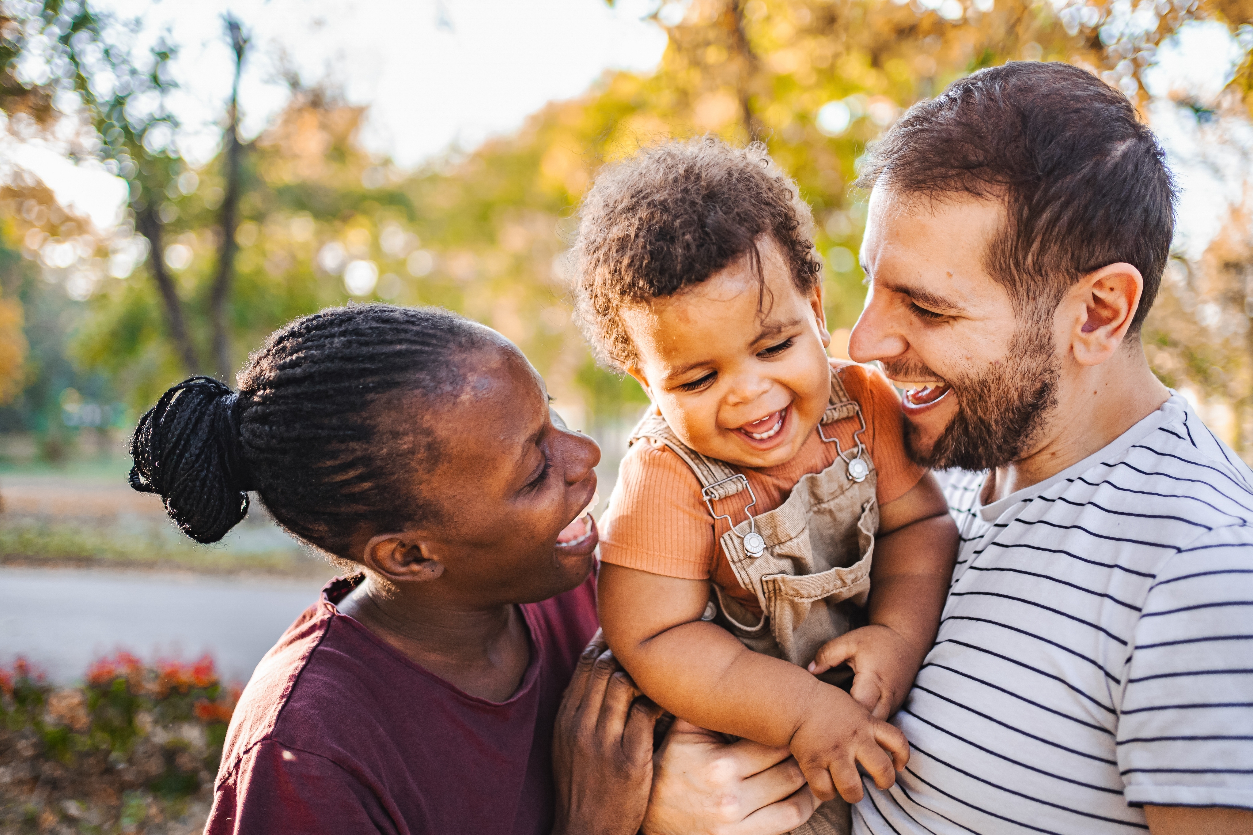 A joyful couple shares a moment outdoors, holding a smiling baby between them, conveying love and happiness