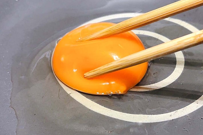 箸で黄身をつかんているフライパン上の生卵。