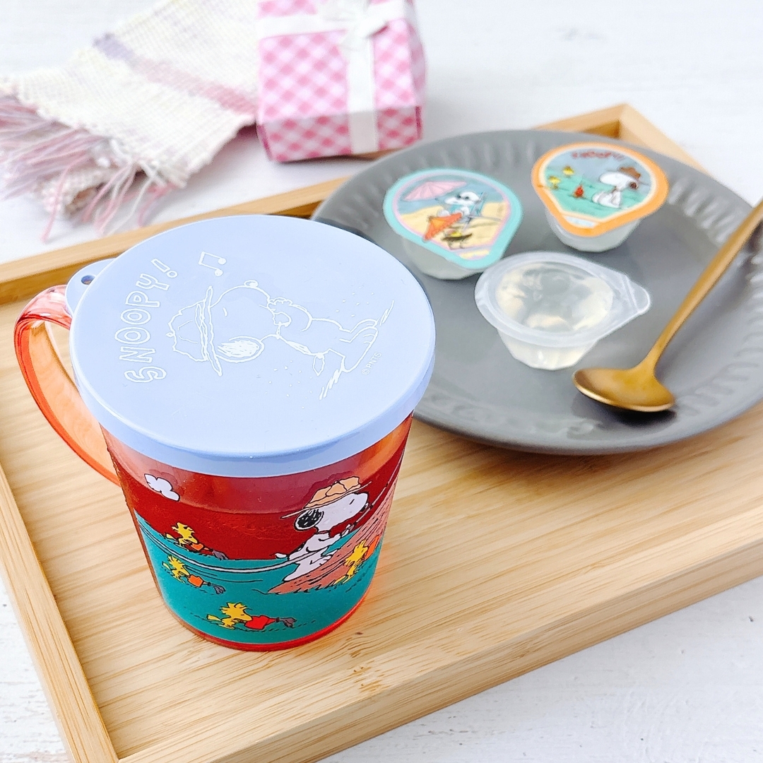 木製トレイの上に、スヌーピーのカップとプリンカップがあり、横に金のスプーンが置かれている。
