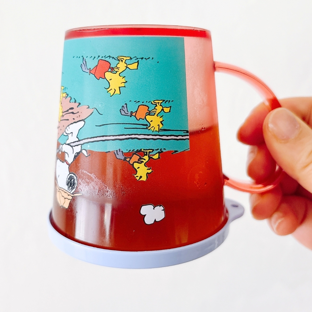 手に持たれたアニメキャラの絵が描かれたカップ。