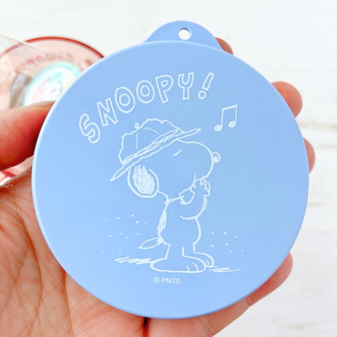 手に持たれたスヌーピーの音符入りデザインの丸いアイテム。
