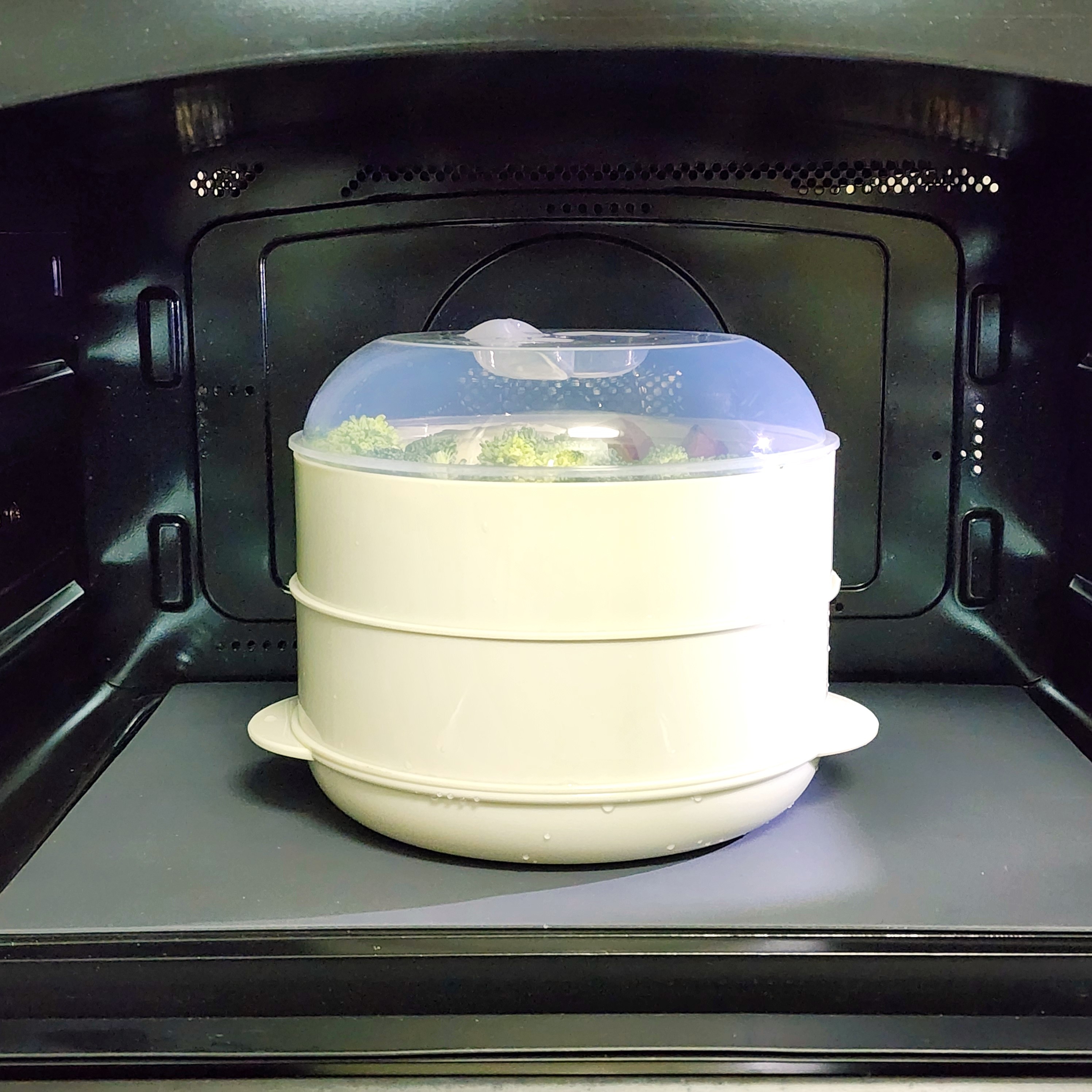 蒸し器がオーブン内に置かれており、野菜が調理中です。