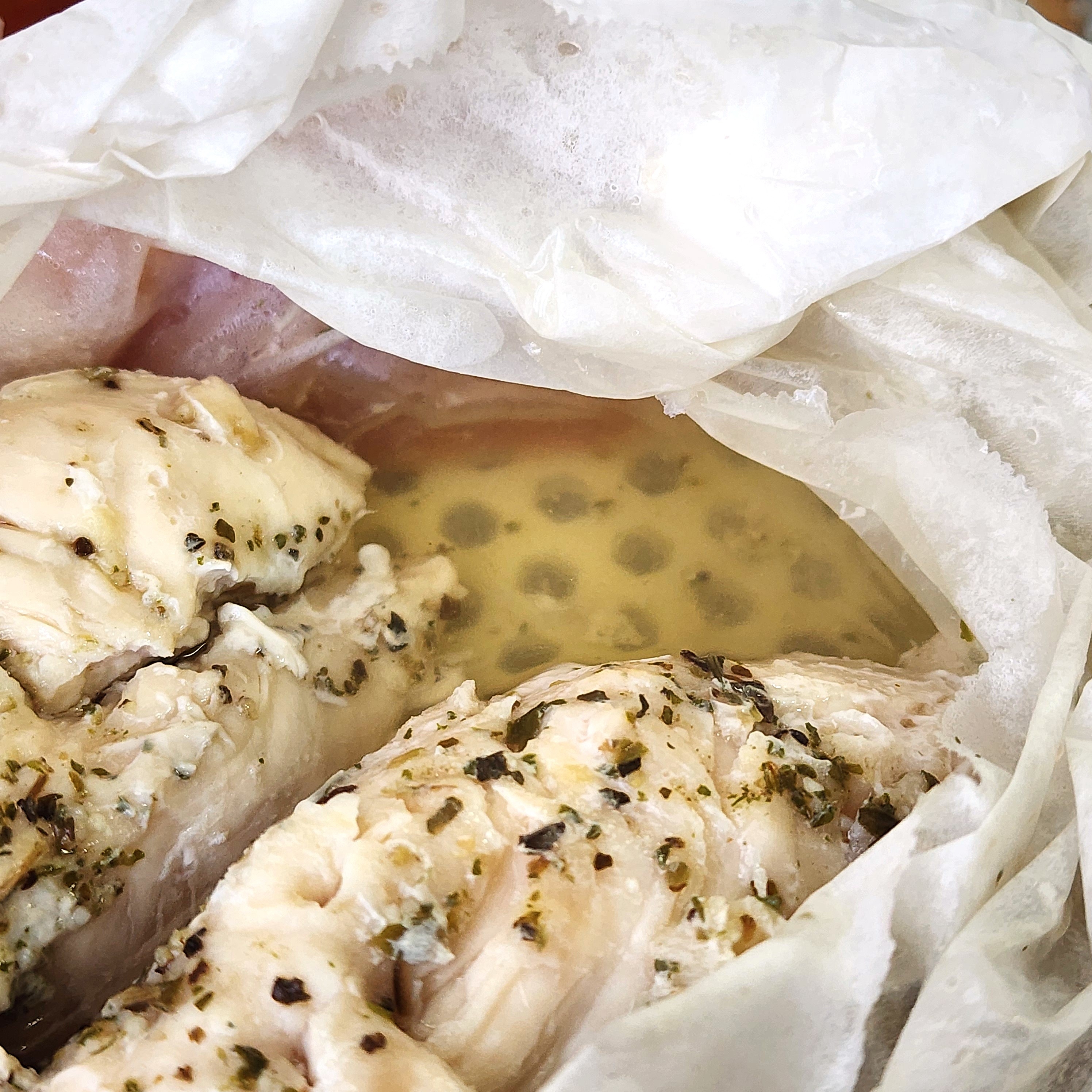 調理されたハーブチキンがペーパーに包まれ、風味豊かなスープが染み出しています。