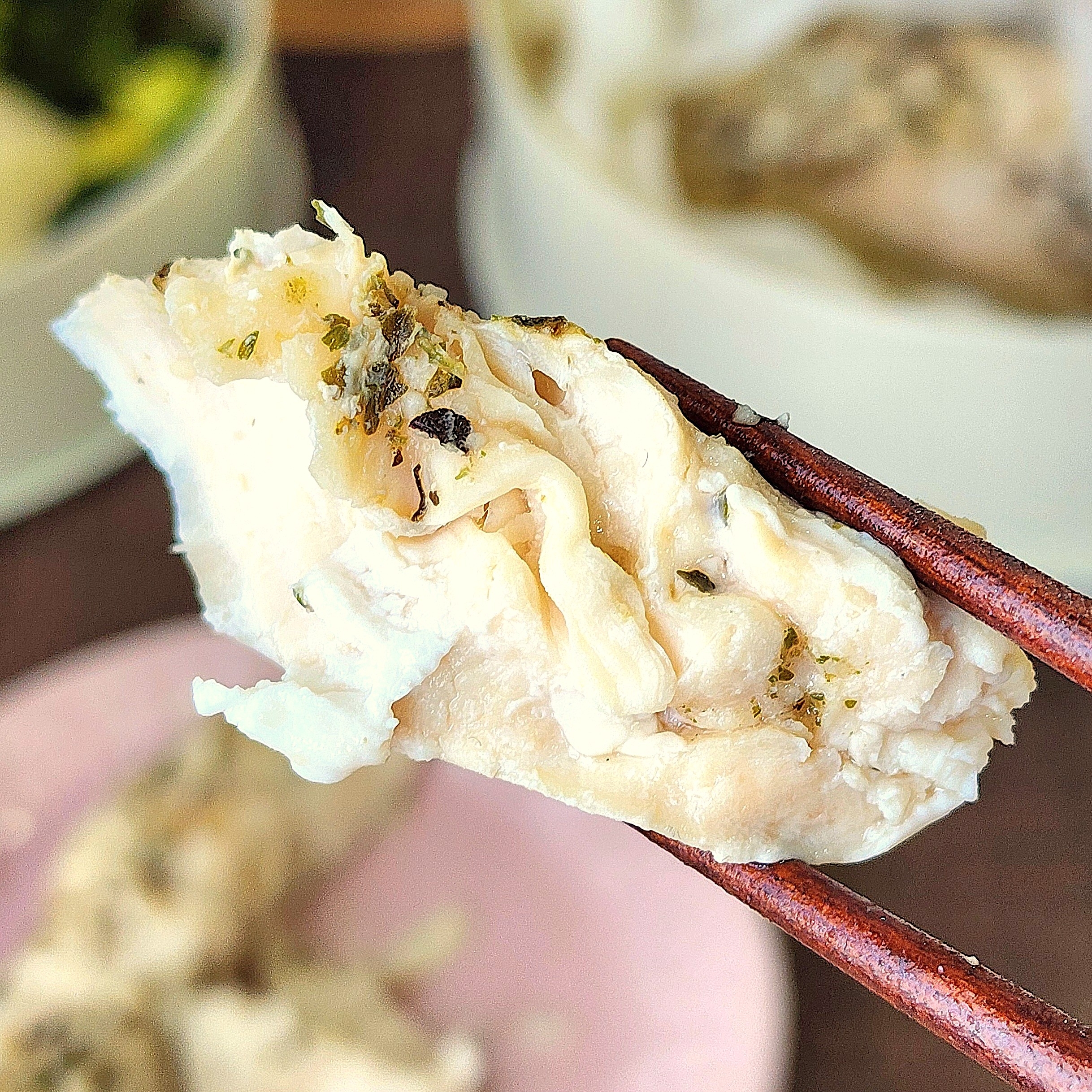 箸で持たれた飲茶の蒸し餃子がクローズアップされた写真。ハーブがトッピングされている。