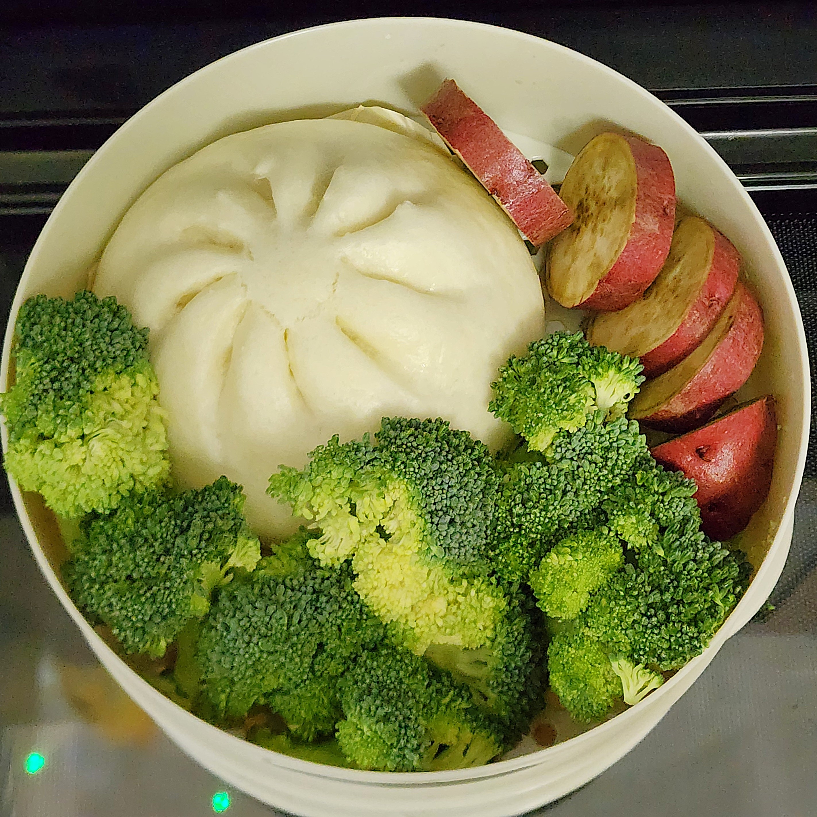 大きな饅頭が容器に入り、ブロッコリーとスライスしたじゃがいもが周りに配置されています。