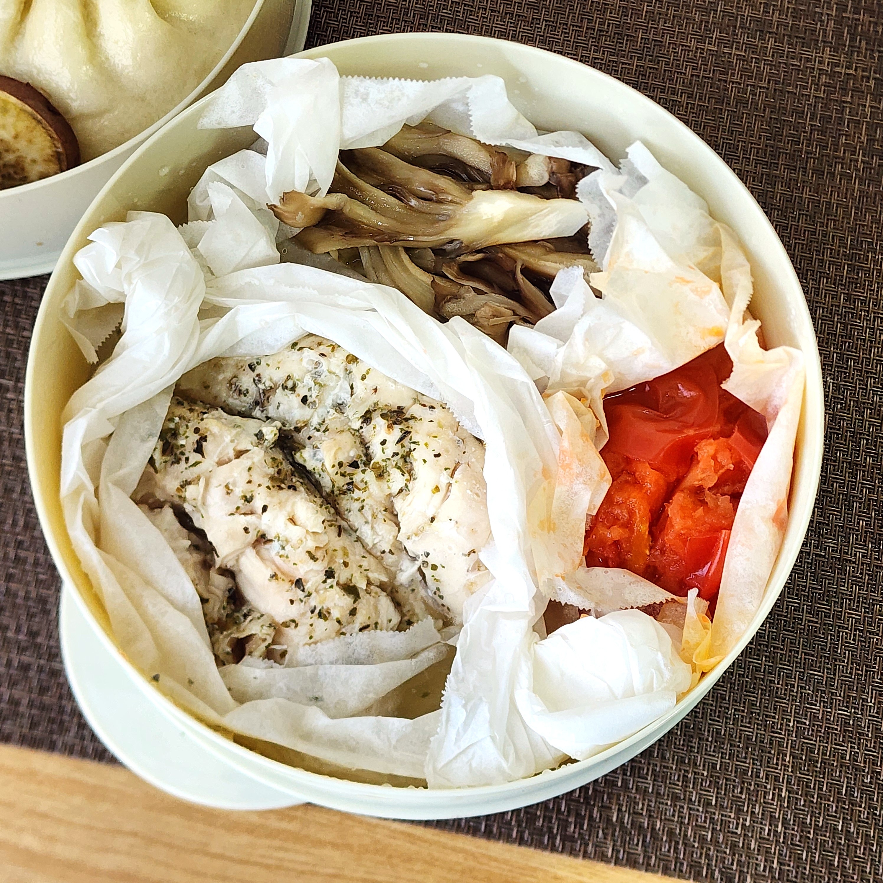 紙で包まれたハーブチキン、きのこ、トマトが入った弁当。