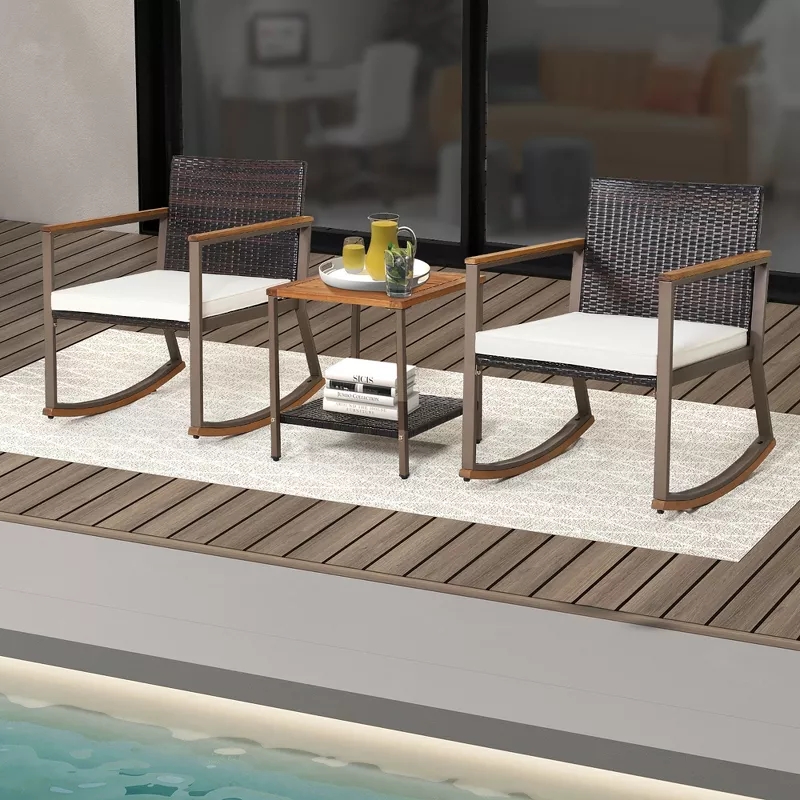 Two wicker rocking chairs with light cushions are on a patio next to a small table holding a pitcher and glasses, overlooking a pool