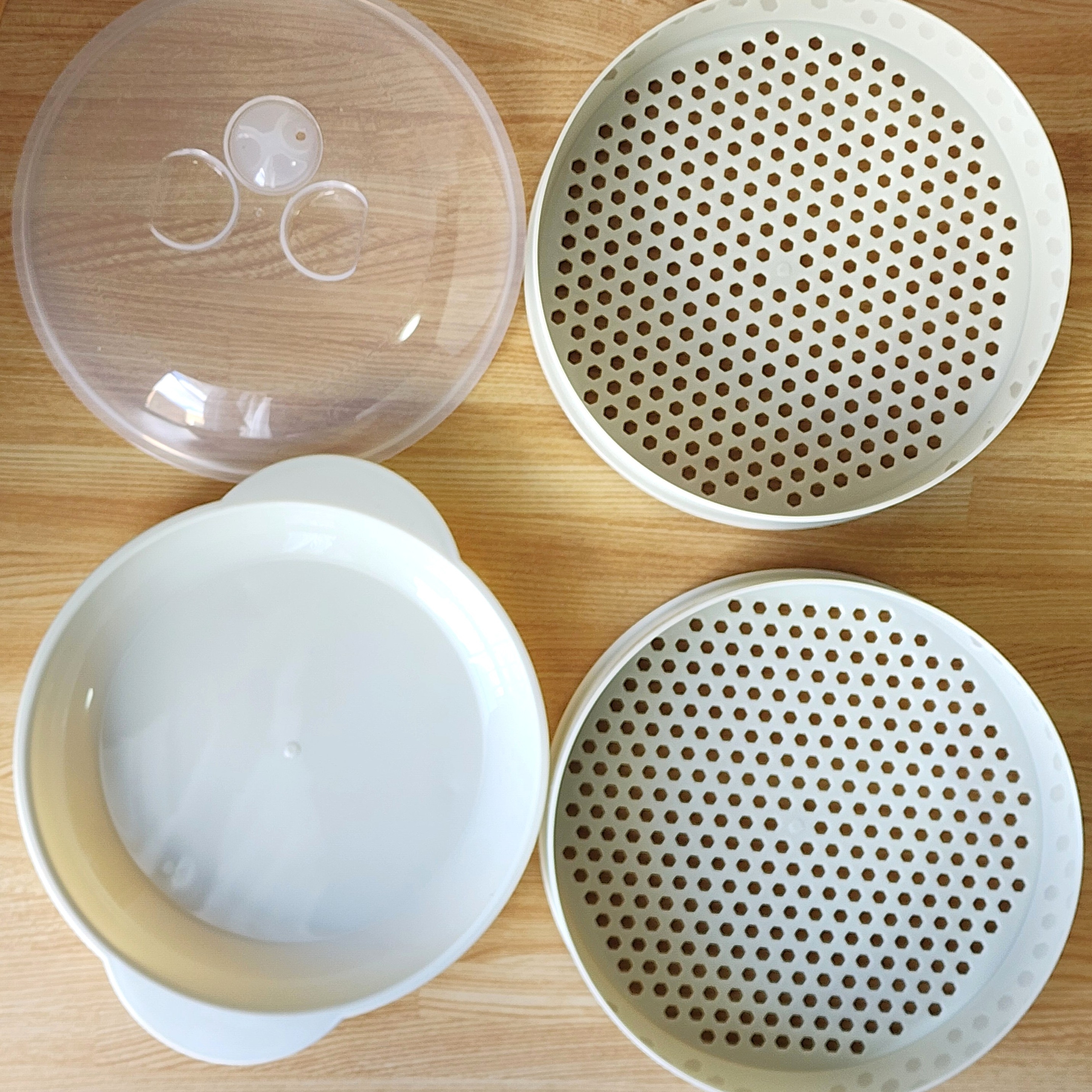 キッチン用品の蒸し器セット。透明な蓋と二つの穴あきトレイ、透明な拭きトレーが含まれている。
