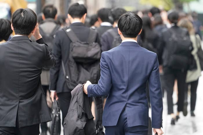 ビジネス街で歩く多くのビジネスパーソン。男性がスーツのジャケットを手に持っている後ろ姿。