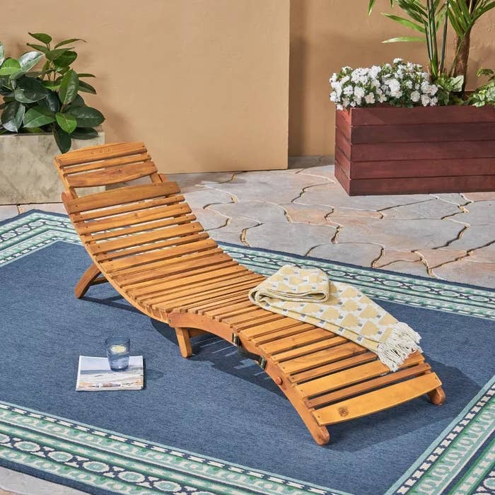 Wooden lounge seat connected a patio, acceptable connected a patterned rug, with a folded broad and a solid of h2o nearby