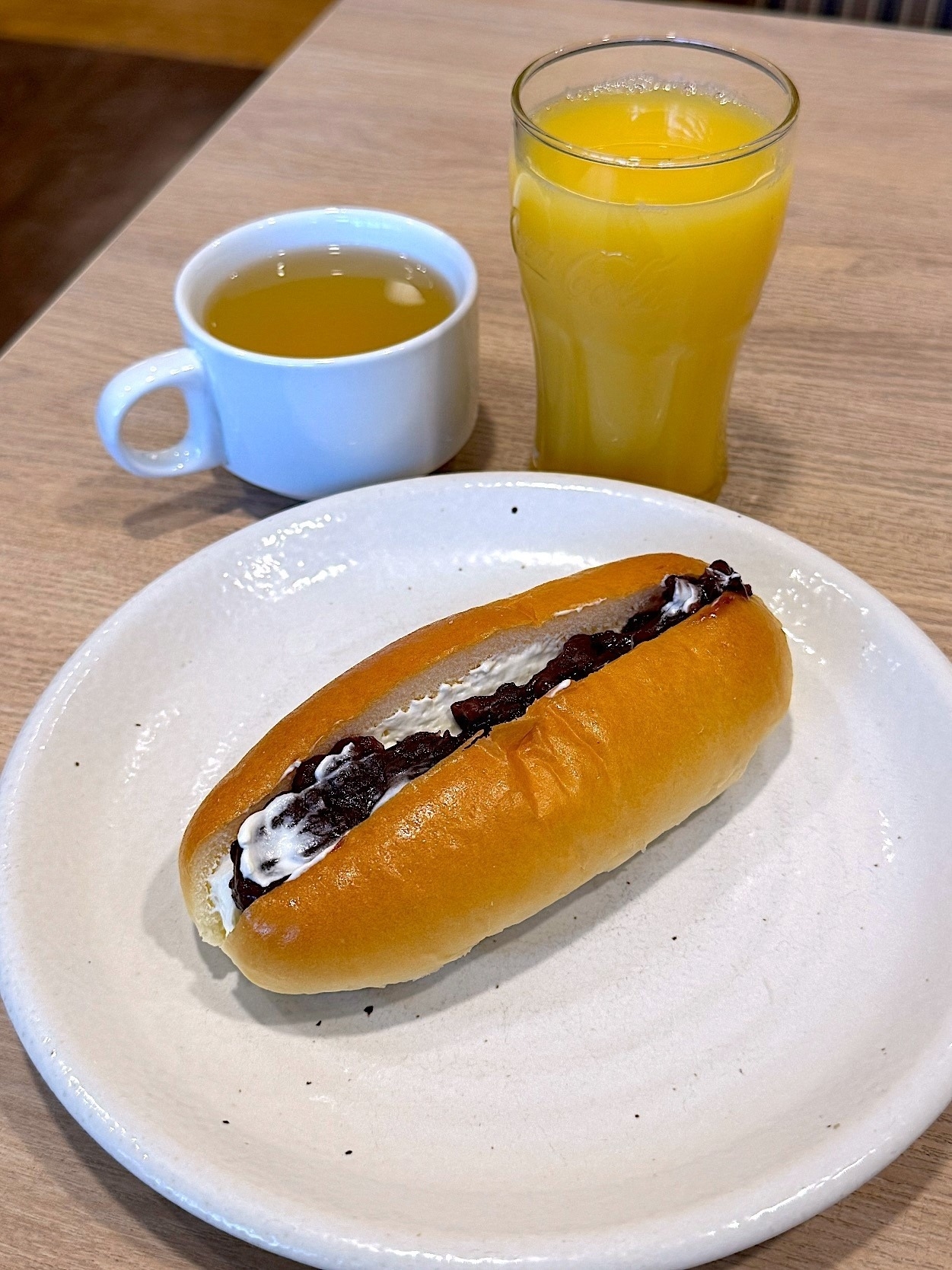 テーブルの上にホットドッグロールにクリームとあんこを挟んだパン、ホットドリンク、オレンジジュースが置かれている。