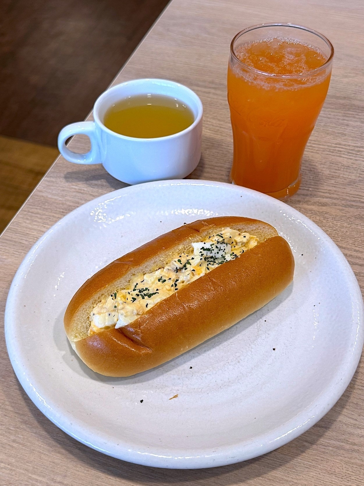 白い皿に卵サラダを挟んだパン、隣にオレンジジュースとカップの紅茶が置かれた食事セット。