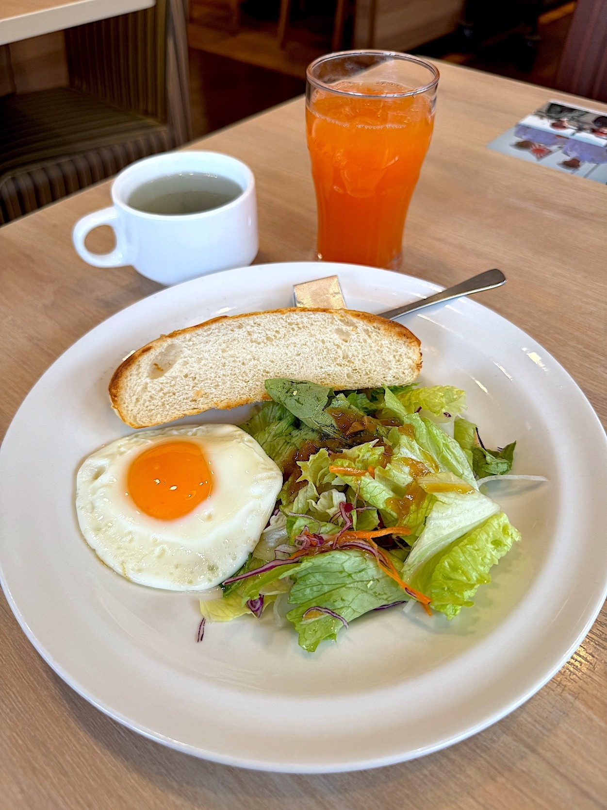 トースト、サラダ、目玉焼きが乗った朝食プレート。オレンジジュースとコーヒーカップがテーブルに置かれている。