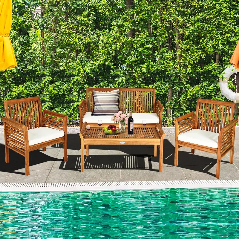 Outdoor wooden patio furniture with cushions arranged around a table by a pool, surrounded by lush greenery