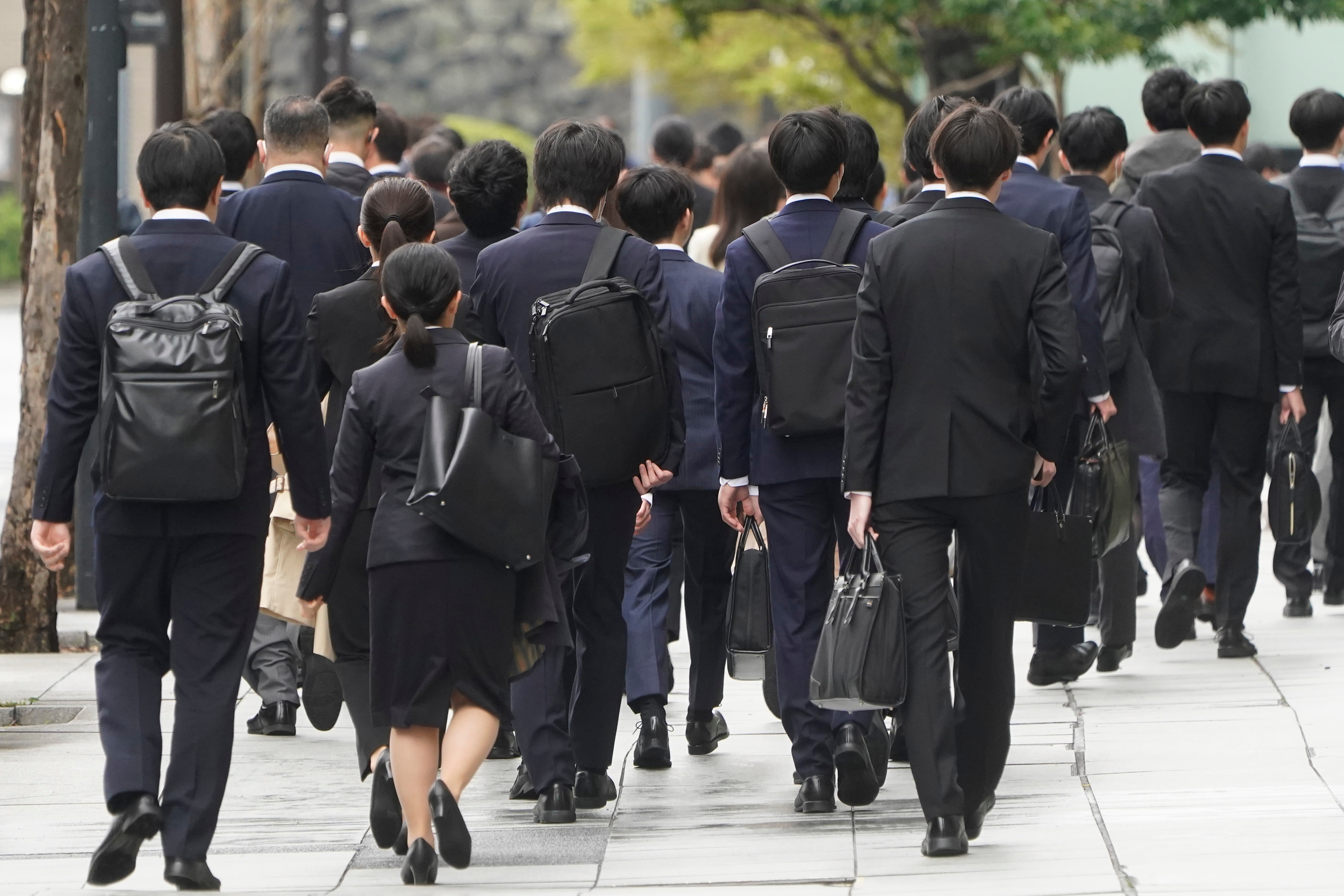 通勤中のスーツ姿のビジネスパーソンたちが歩道を歩いている様子。