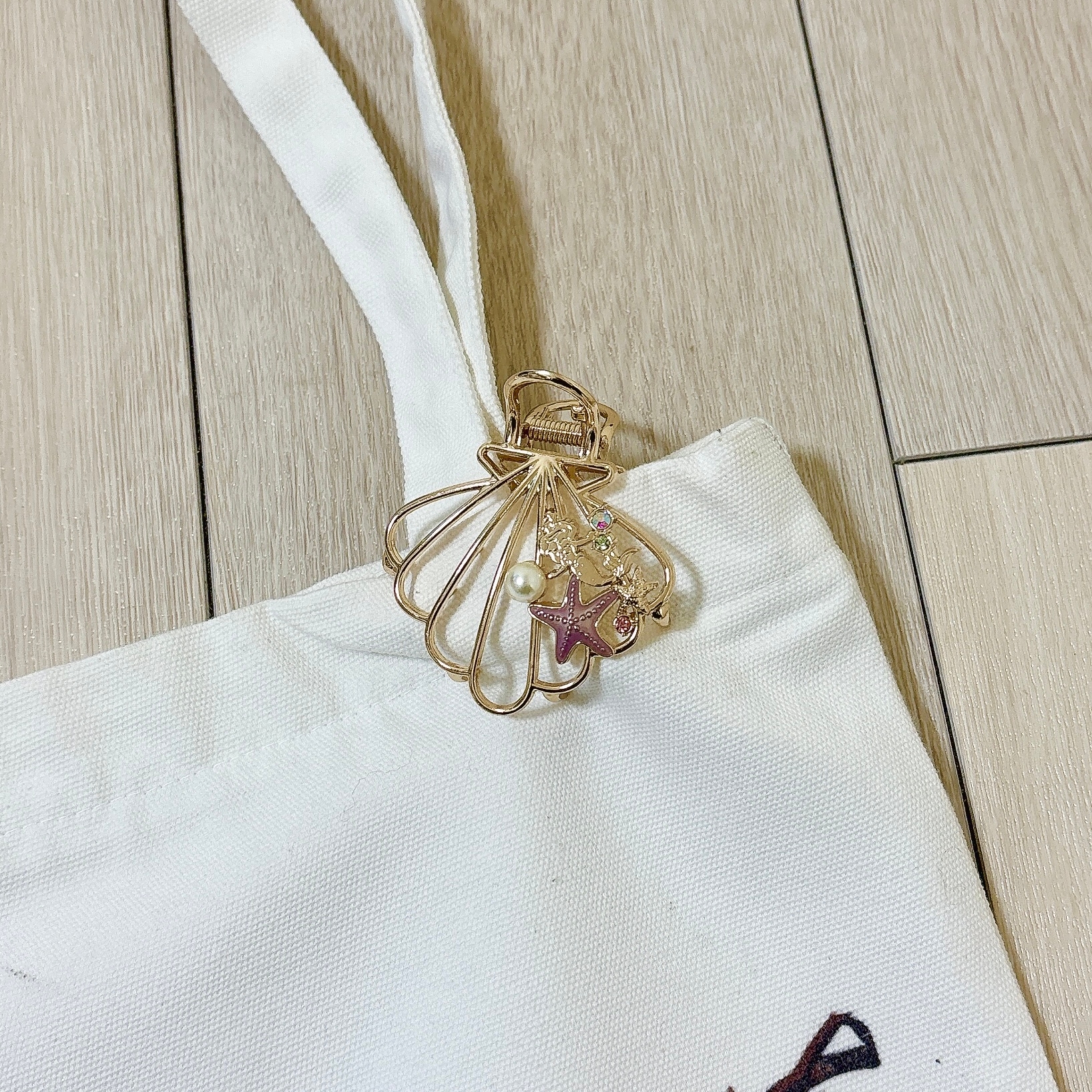 トートバッグの持ち手部分に、貝殻と星型の装飾が施された金色のアクセサリーが付いている様子。