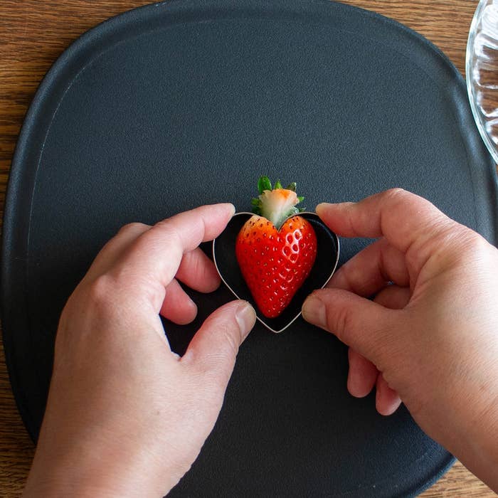 ハート型カッターでいちごを形作る手元。黒いプレートの上。